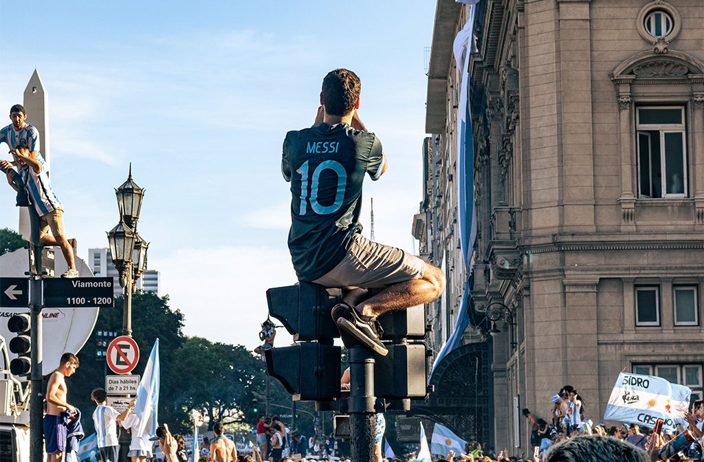 Crowd celebrating in Buenos Aires after Argentina's 2022 World Cup win with a fan in a Messi shirt climbing a lamp post Image: Fabrizio Velez/Pexels