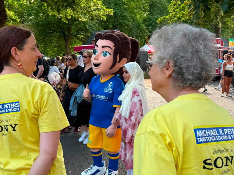 Nettie the mascot taking photos with people at the Michael R Peters stand Bedford River Festival 2026