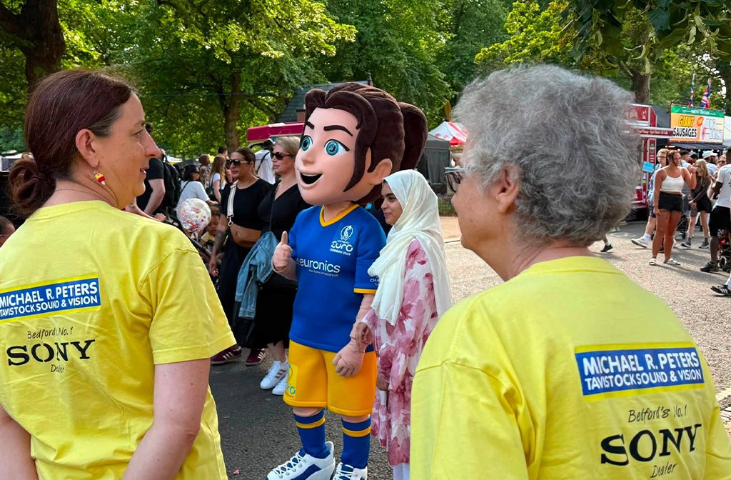 Nettie the mascot taking photos with people at the Michael R Peters stand Bedford River Festival 2026