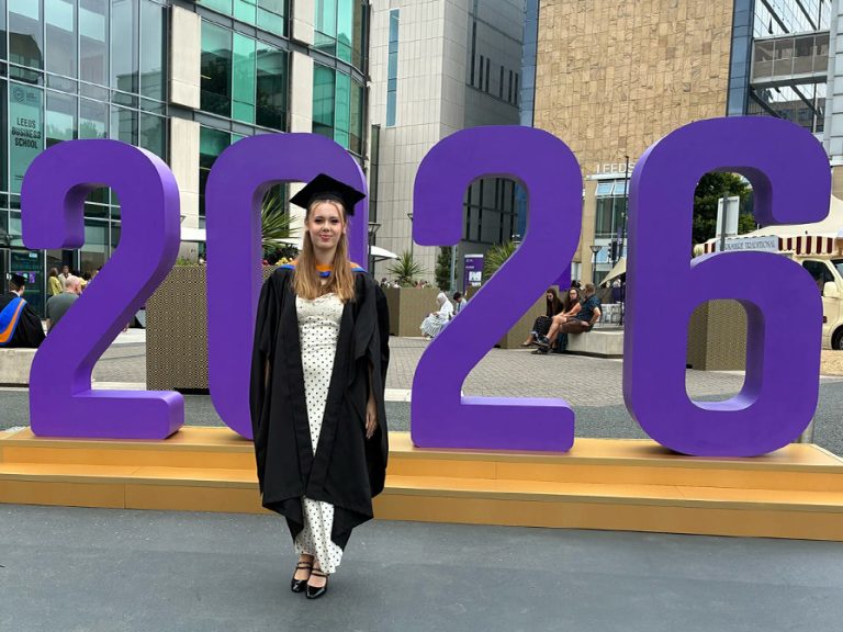 Sophie Stapley on her graduation in her graduation cap and cloak standing in front of a large 2026. day Image: The Stapley family.
