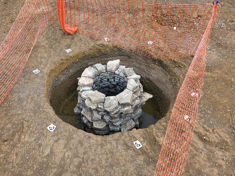 A stone circular well, inside a deeper hole, cordoned off by orange netting, shows where archeologists have found a well, believed to be from the 1870s, uncovered at the construction site for Universal United Kingdom Resort Image Project Universal