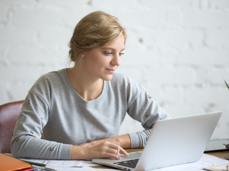 A woman sitting at a desk at work on a laptop. Image Magnific