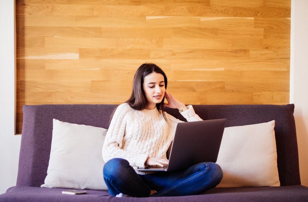 A woman sitting cross legged on a sofa while working on a laptop. Image Magnific