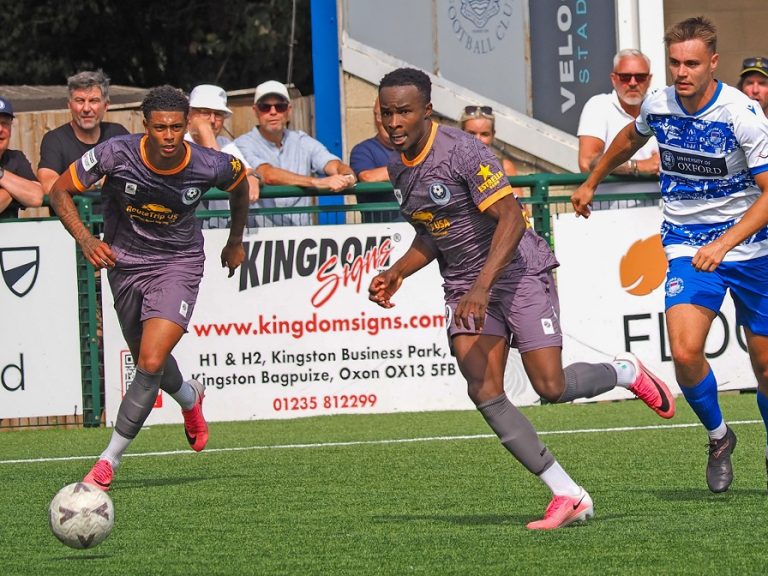 A Bedford Town player in away kit takes the ball away from an Oxford City player