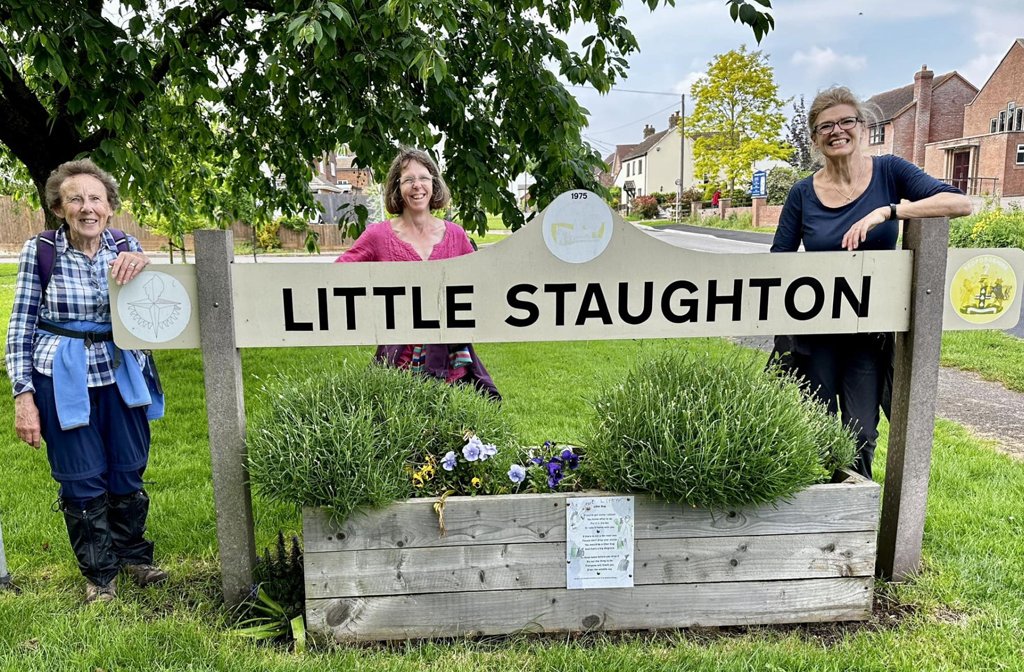 Three members of the North Bedfordshire Ramblers group posing around the commemorative 1951 Festival of Britain village sign