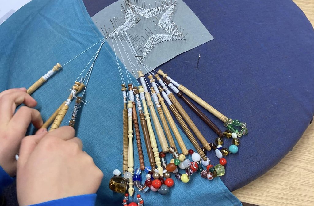 Young lacemakers using bobbins on a cushion with the Aragon Lacemakers