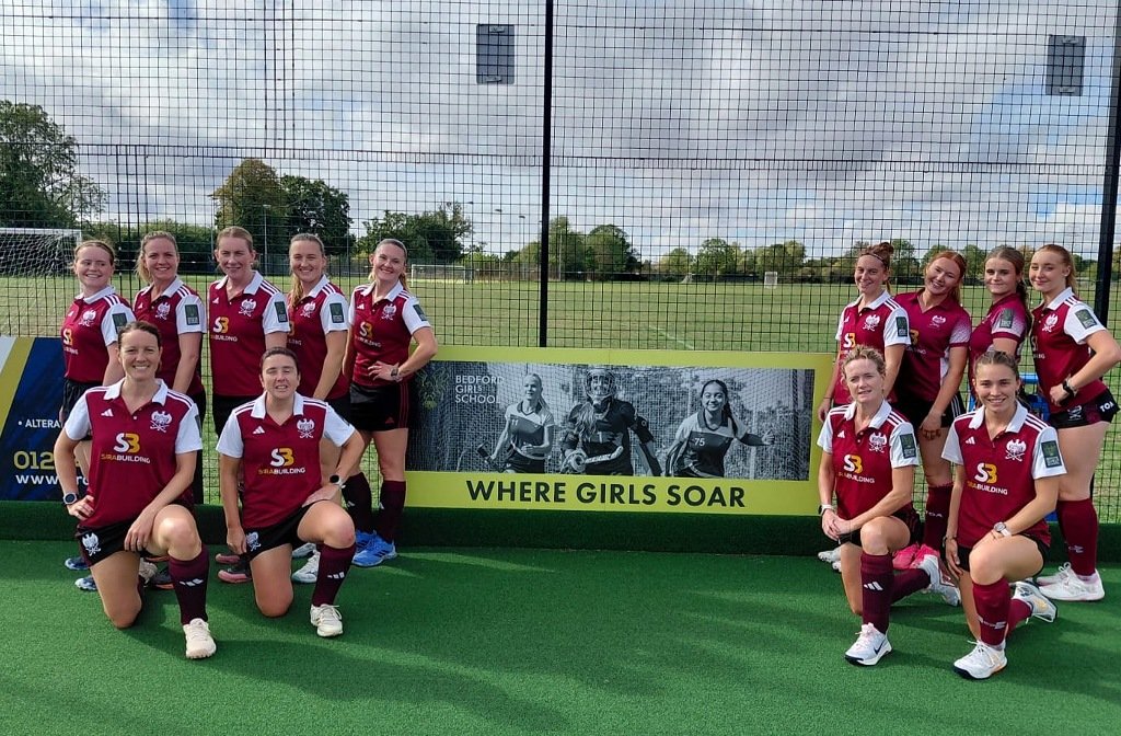 A group of Bedford Hockey Club players either side of a Bedford Girls' School advertising banner