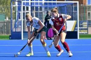 Two hockey players battle for the ball on the blue-clad surface of Chester Road